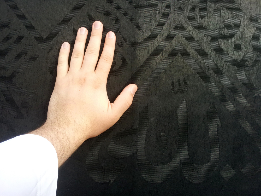 Kaaba Mecca in Saudi Arabia and Muslim pilgrims coming for Hajj, male hand touching the black Cover